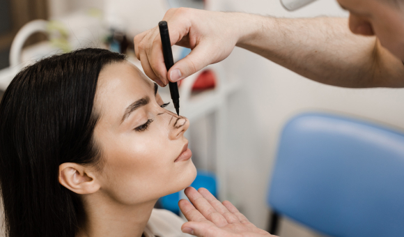 Close-up of a surgeon drawing precise lines on a woman's nose, marking the areas for a rhinoplasty procedure