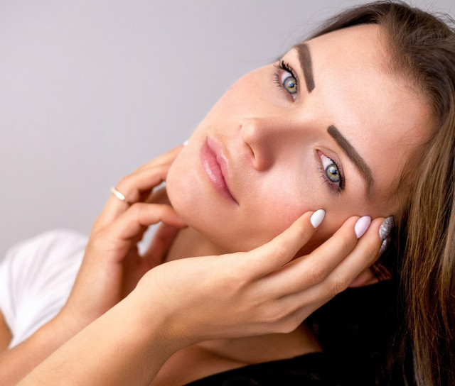 A woman holding her face with both hands, highlighting her smooth, glowing skin