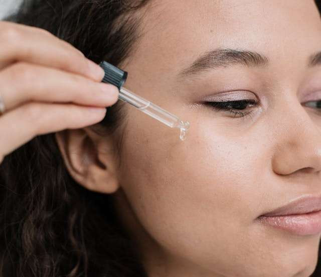 Close-up of a woman applying serum to her face, with a dropper releasing the product onto her skin