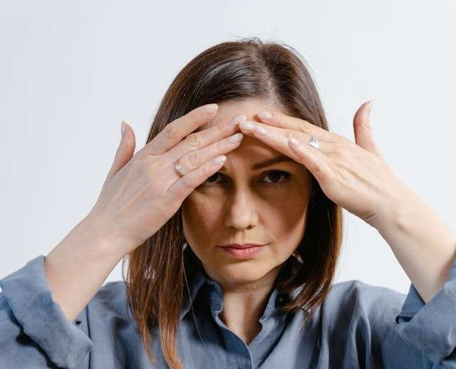 Close-up of a woman touching her hairline with both hands, framing her face